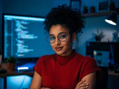 Confident young woman programmer in glasses working late at night with code on screen.