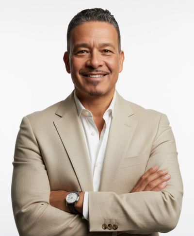 Confident man in beige suit smiling with arms crossed against white background.
