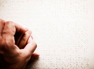 A person reading Braille with their fingers on a white page.