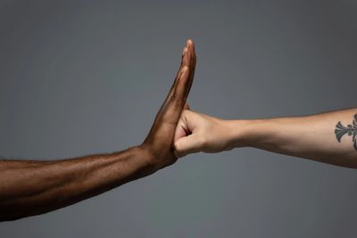 A fist meeting an open hand in a neutral gray background.