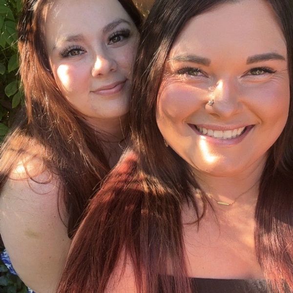 Two smiling women enjoying sunlight outdoors, close-up selfie.