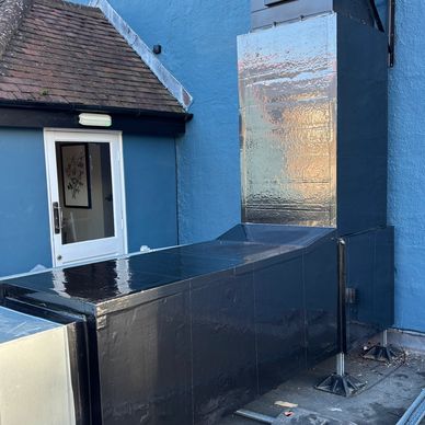 Large black industrial ventilation or air conditioning unit attached to a blue building.