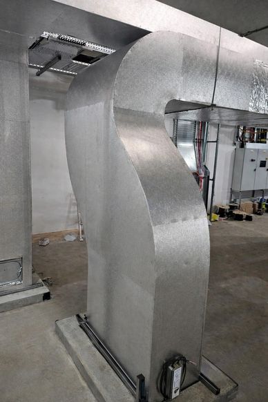 Large metallic HVAC duct with a curved section in an industrial setting.