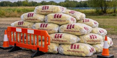 Stacked bags of insulation material with safety cones and barrier outdoors.