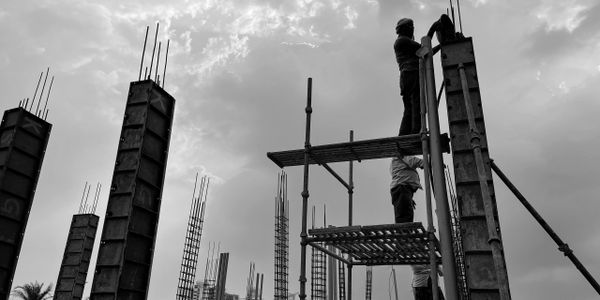 Construction workers on scaffolding working on building columns under cloudy sky.
