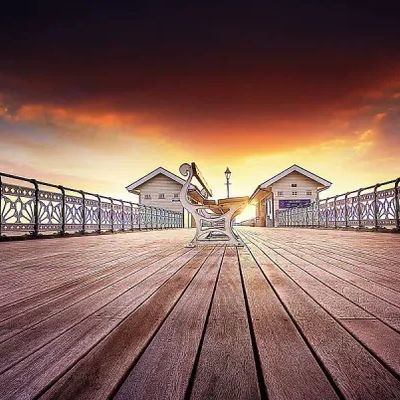Empty bench on a wooden pier at sunset with ornate railings.