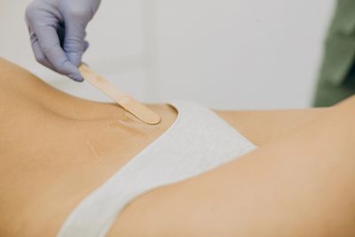 A person applying wax on the lower abdomen for hair removal.