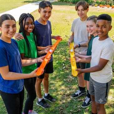 Six kids playing a team game outdoors with colorful tubes.