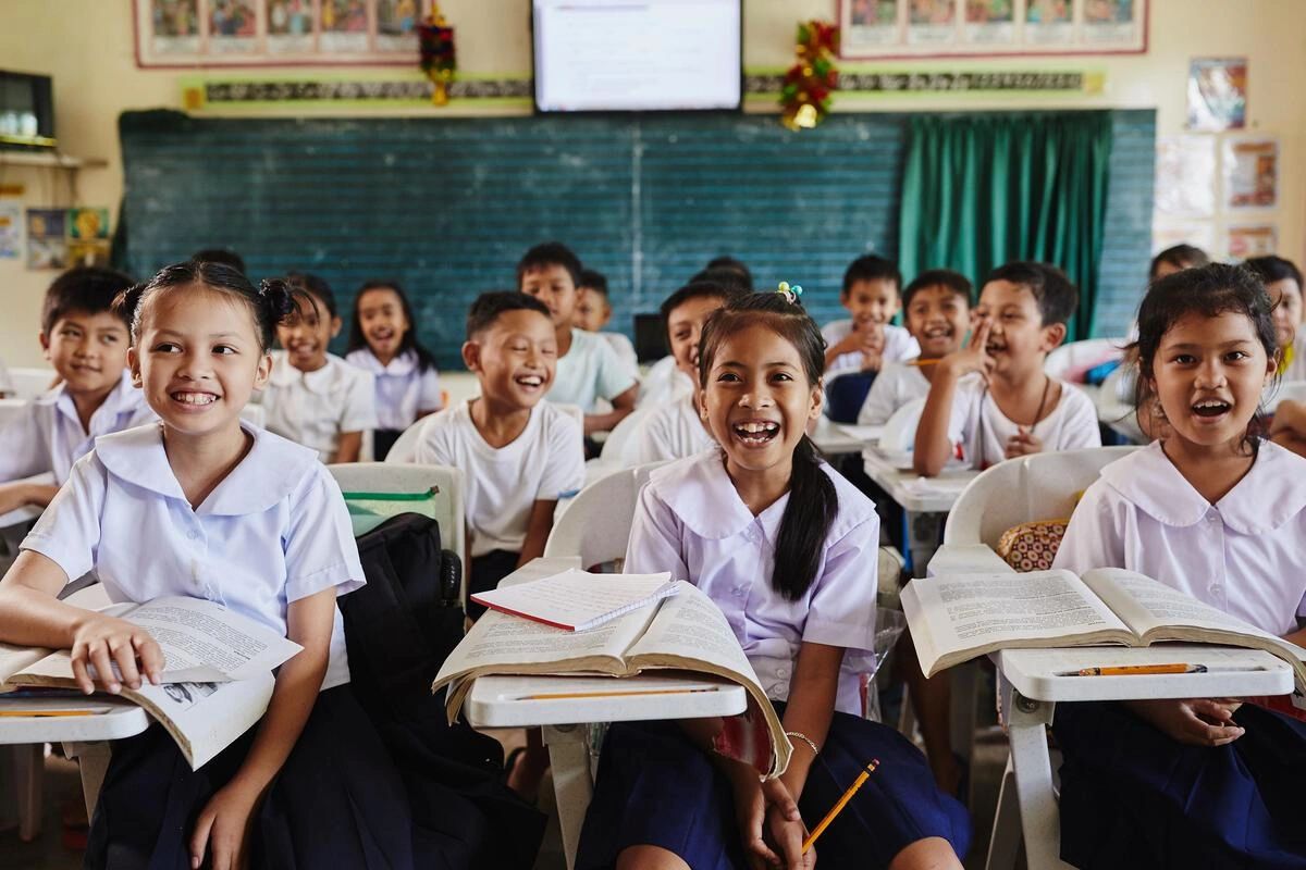 Happy schoolchildren in uniform sitting in a classroom with open books.