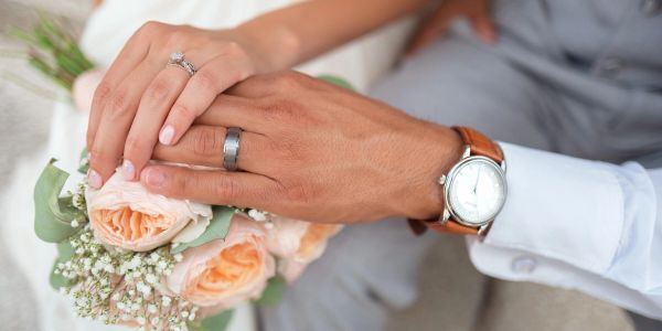 Couple's hands with wedding rings over a bouquet of flowers.