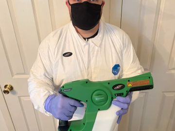 Person in protective gear holding a green disinfection sprayer.