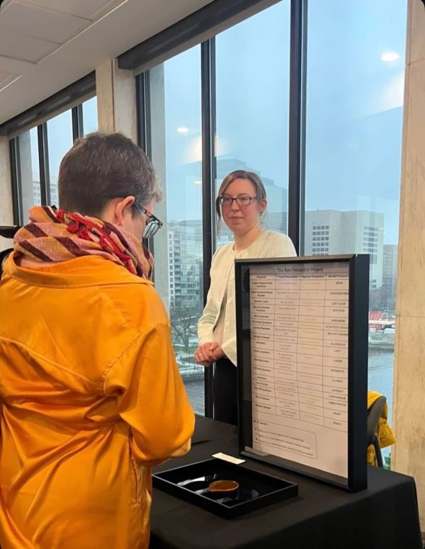 Two women at an indoor event, one presenting a project display board.
