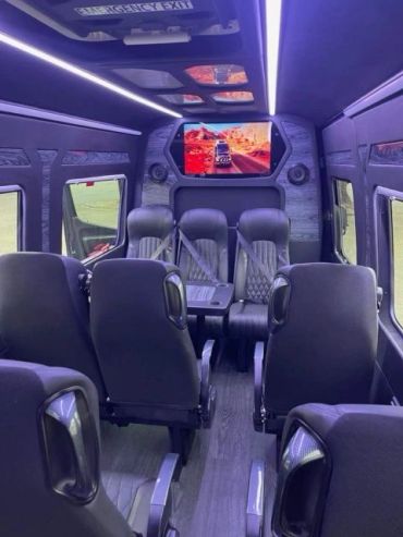 Luxurious black leather seats inside a modern passenger van with a TV screen.