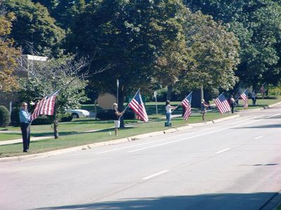 People standing in a line holding American flags along a street.