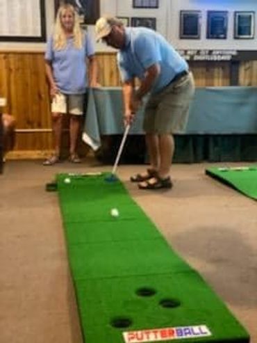 Man putting on an indoor mini-golf green while a woman watches.
