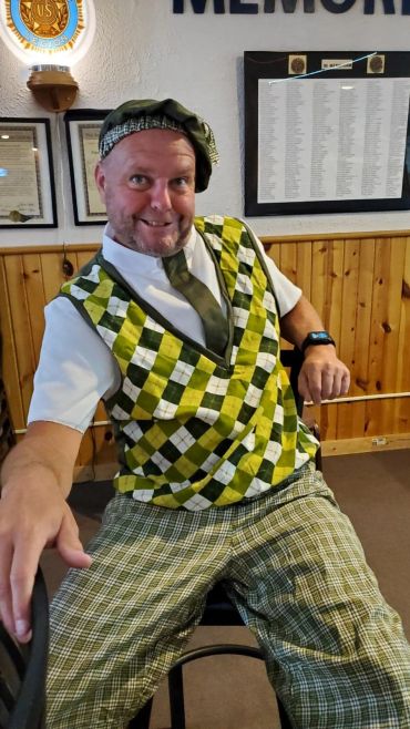Man in mismatched green plaid outfit posing indoors with playful expression.