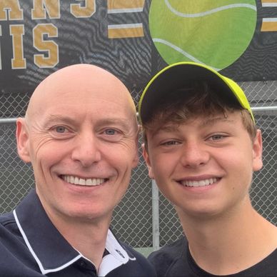 Two smiling males posing at a tennis court.