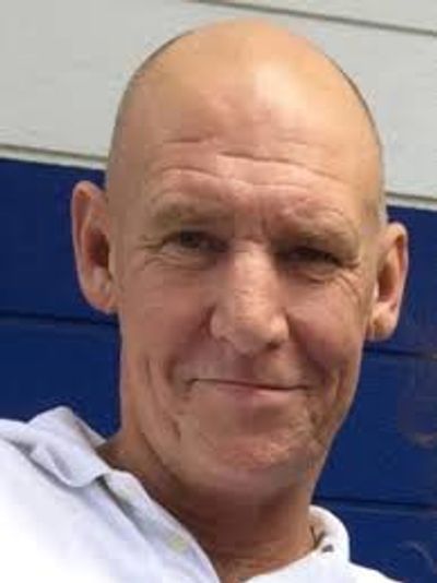 Smiling bald man in a white shirt with a blue and white background.