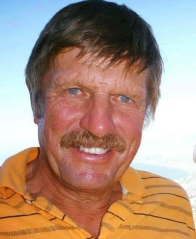 Smiling man in an orange striped shirt with blue eyes and a mustache.