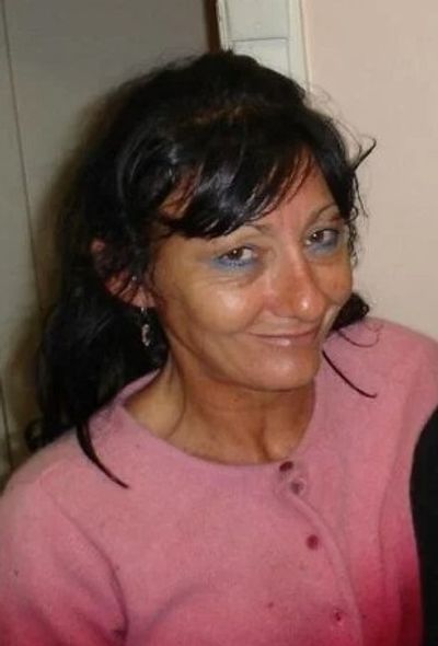 Woman with dark hair wearing a pink sweater, smiling slightly.