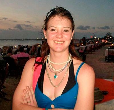 A smiling woman in a blue swimsuit at a beach during sunset.