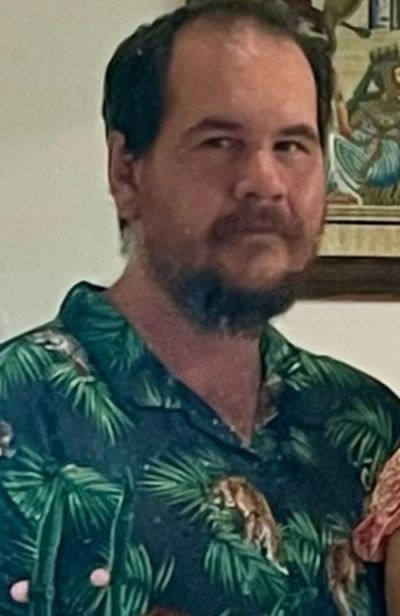 Man with a beard wearing a green tropical shirt indoors.