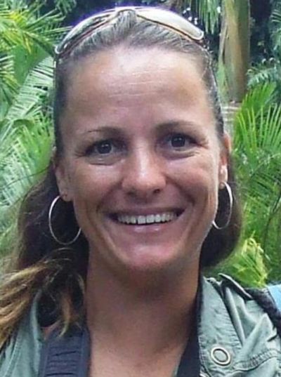 Smiling woman outdoors with sunglasses on her head and hoop earrings.