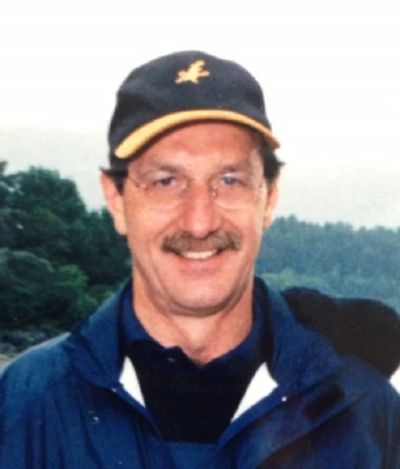 A man smiling outdoors wearing a cap and glasses.