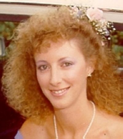 Smiling woman with curly hair and floral hair accessory.