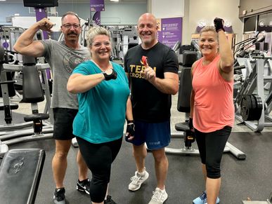 Four people flexing and smiling in a gym.