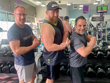 Three men posing with flexed muscles in a gym.