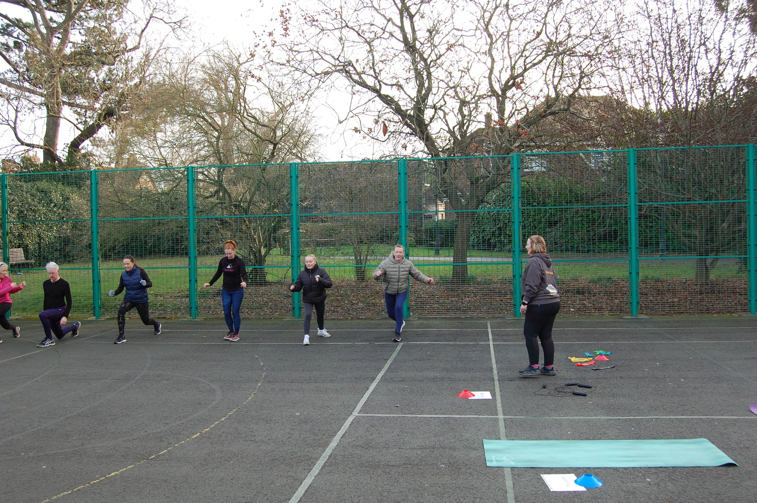 A group of people doing fitness exercises outside with a trainer