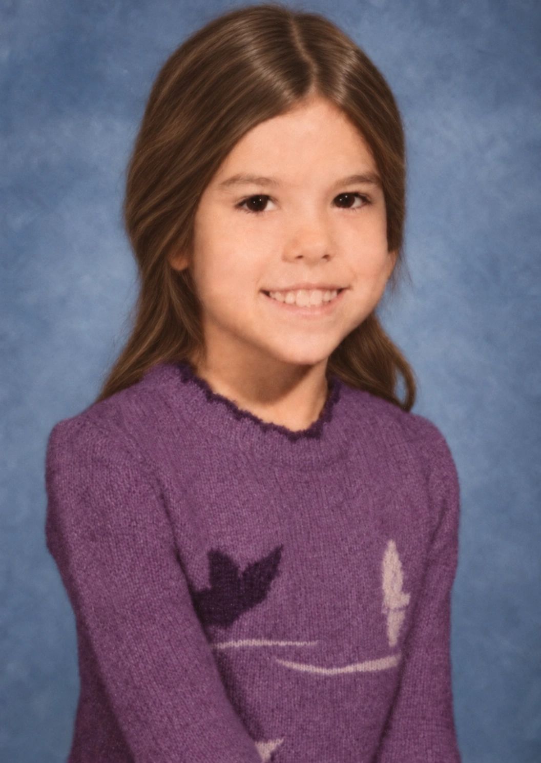 Young girl smiling in a purple sweater against a blue background.