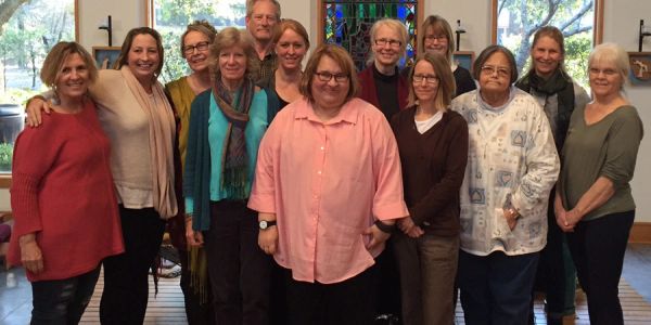 A group of thirteen adults standing indoors, smiling at the camera.