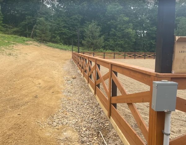 A wooden fence borders a gravel and dirt pathway near a wooded area.