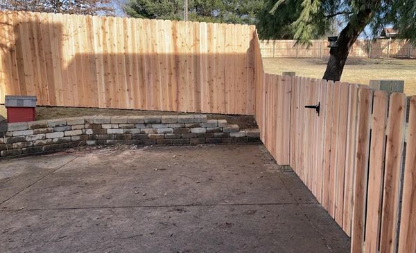 Newly installed wooden fence and stone retaining wall in a backyard.