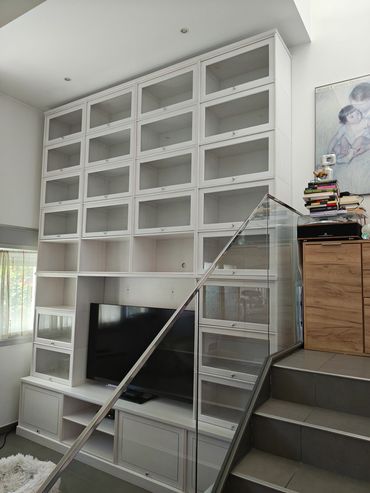 Modern white shelving unit with TV and glass stair railing.