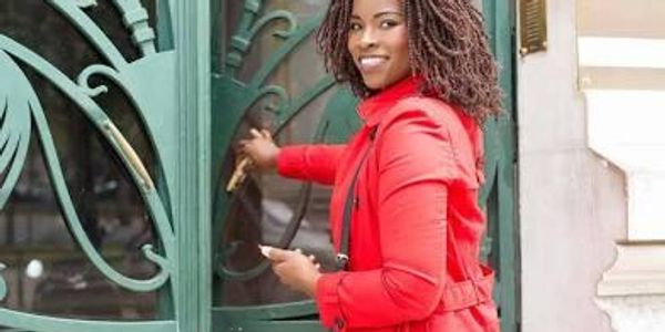 A smiling woman in a red coat opening a decorative green door.