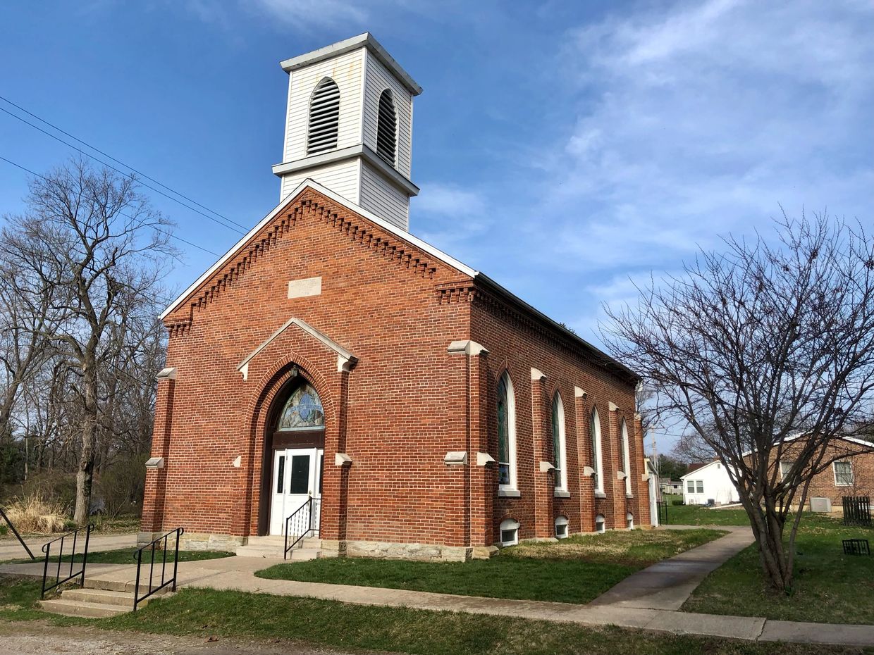 Brick building with steeple and stained glass windows.