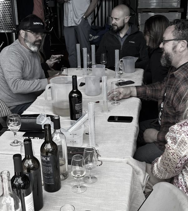 Group of people tasting wine around a table with bottles and glasses.