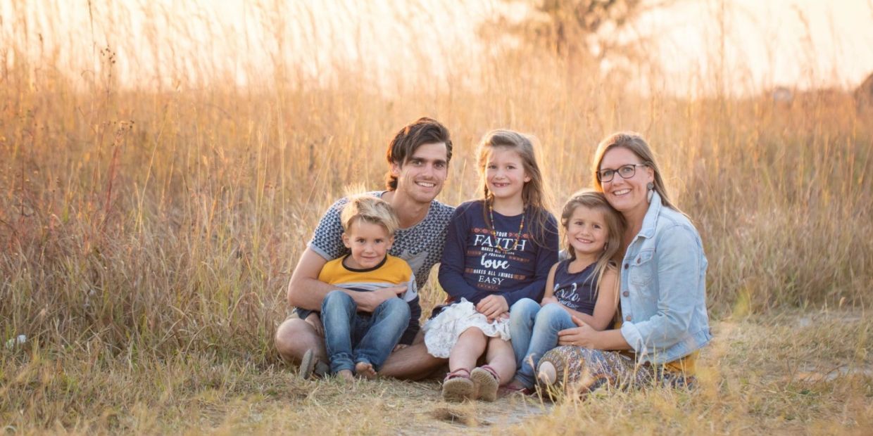 A warm family moment with two adults and three children sitting in a field at sunset.