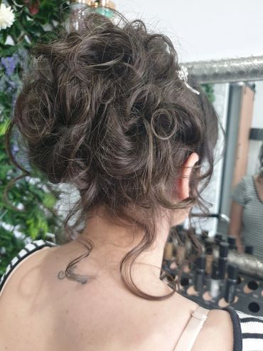 Intricate curly updo hairstyle with loose strands.