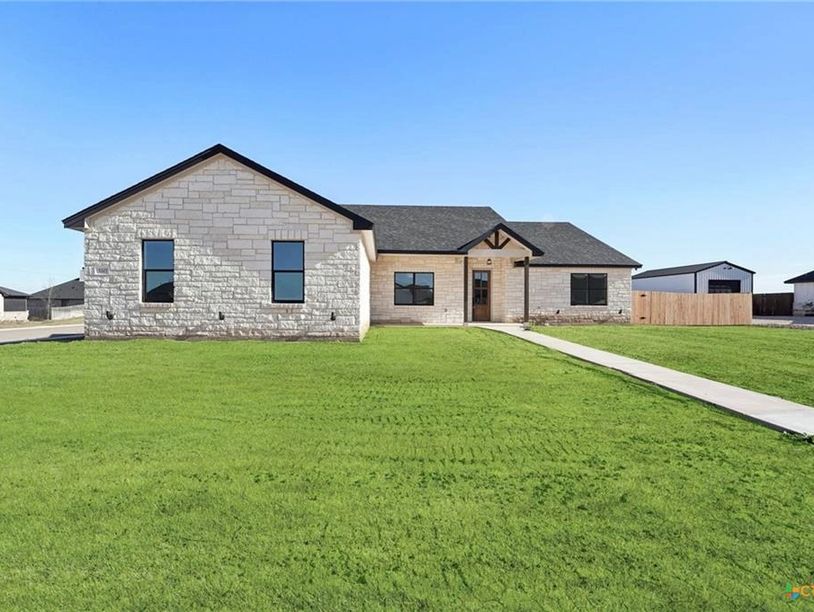 Modern single-story house with stone exterior and large green lawn.