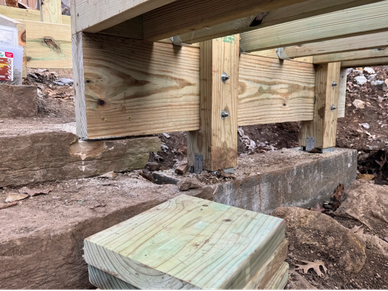 Close-up of wooden deck support structure over concrete and stone.