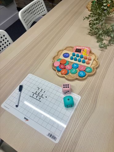 A math learning setup with a whiteboard, dice, and colorful wooden numbers on a table.