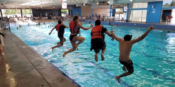 Four people jumping into an indoor swimming pool.