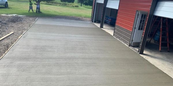 Freshly poured concrete driveway beside a red garage.