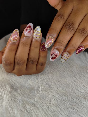 Hands with artistic nail designs featuring gold lines and flower patterns.