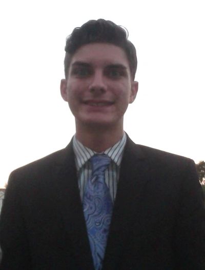 Young man in a suit with a patterned blue tie smiling at sunset.