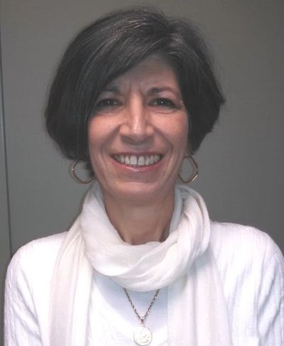 Smiling woman with short dark hair wearing a white scarf and earrings.